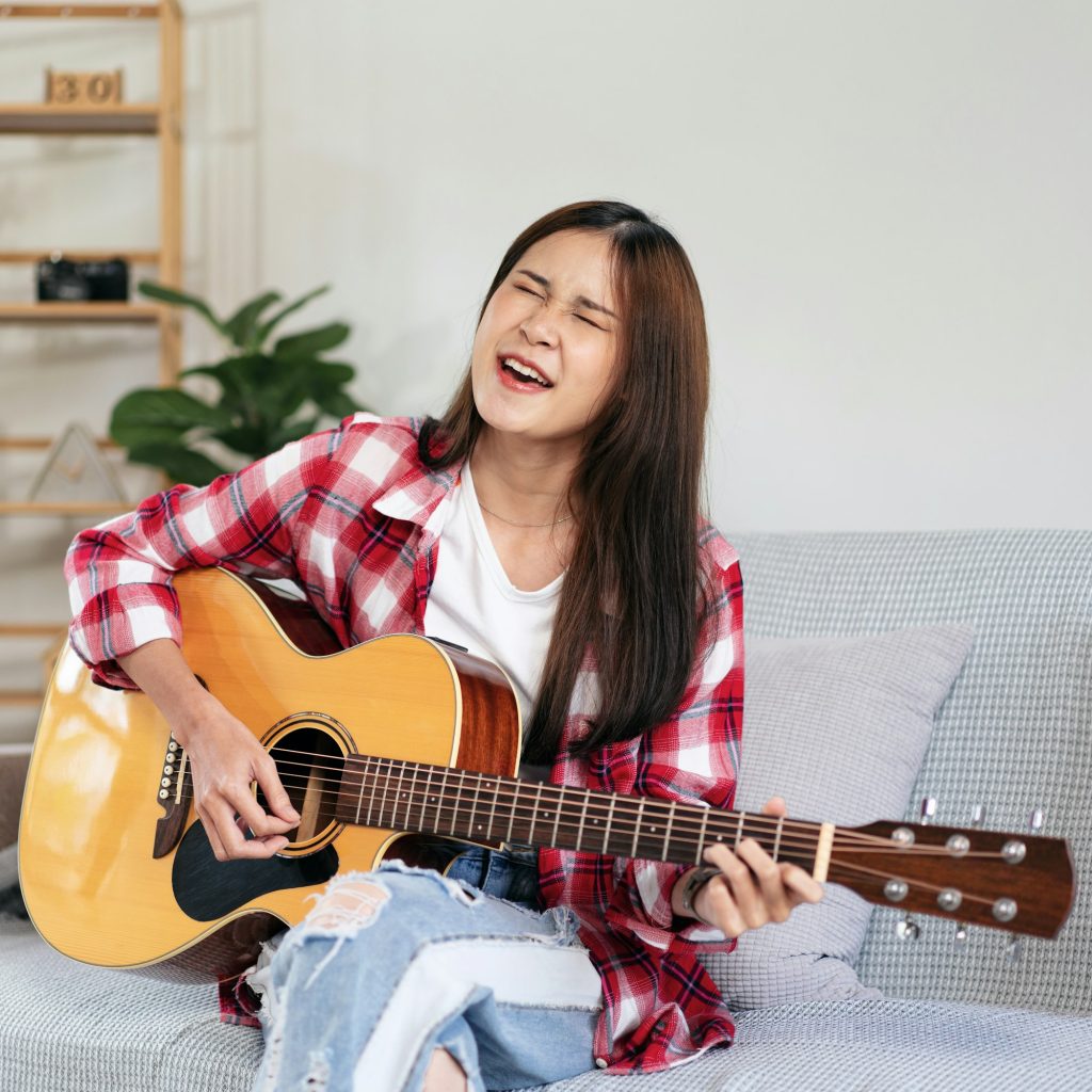 Young woman is playing guitar and practice to singing the song w